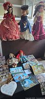 Group shot showing three large dolls, two small Madame Alexander dolls, postcard booklet with loose cards, and wooden heart plaque