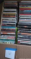 Box filled with rows of CD jewel cases showing spines