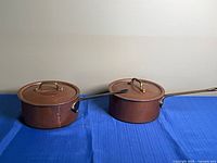 Two lidded copper saucepans side by side, full view