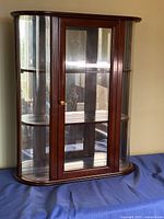 Full front view of curio cabinet showing wood frame, glass door, curved glass sides