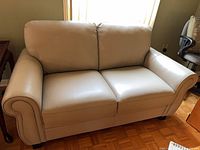 Front view of creamy white leather loveseat showing cushions, arms, feet