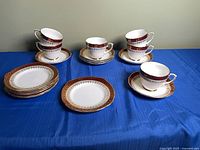 Full view of 6 cup and saucer sets plus stack of 5 luncheon plates on blue cloth