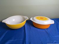 Orange oval casserole with sunflower lid beside yellow round casserole
