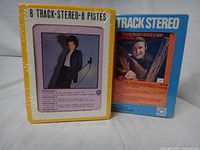 Front view of both sealed 8-track cartridges showing cover art and shrink wrap