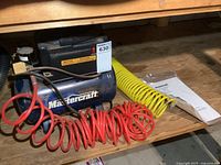 Air compressor with red hose, yellow hose and manual on shelf