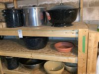 Shelved view showing three enamel pots, stainless bowl, terracotta bowl and two stoneware bowls
