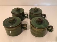 Set of four matching green ceramic lidded soup bowls with handles