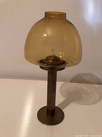 Three-quarter view of brass candle holder with amber glass globe
