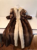 Front view of full-length brown fur coat with cream fur trim