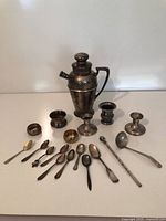 overall view of cocktail shaker, flatware, candlesticks, goblet, small dishes