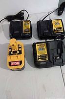 Three DeWalt chargers and one Ryobi 18V battery on surface