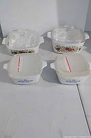 Four Corning Ware dishes with lids, showing two vegetable pattern with glass lids and two blue floral with plastic lids