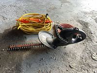 Electric chain saw with yellow coiled extension cord on orange reel and red extension cord