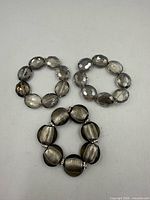 Two faceted grey oval bead bracelets and one flat round metallic grey bead bracelet