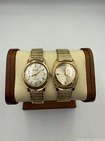 Two gold-tone Bulova watches on stand