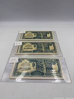 Three of the banknotes in protective sleeves, each showing the face design of the Ten Dollars note