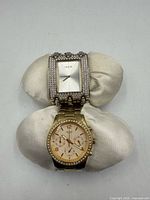 Both Guess watches on cushion, top view showing faces and bracelets