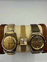 Front view of three gold-tone wristwatches on display pillow
