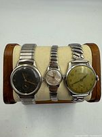 Front view of three stainless steel wristwatches on display stand