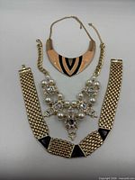 Three necklaces laid out: collar with black enamel, bib with pearls/rhinestones, wide mesh choker with black enamel triangles