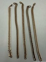 Five gold-tone bracelets laid flat showing link styles
