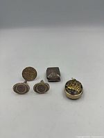 Front view of all five items: round cufflink/tie tack, pair of oval cufflinks, hinged pill box, oval locket