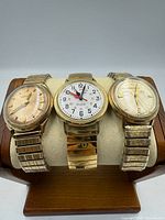Three gold-tone Accutron watches on padded stand showing dials and bracelets