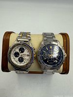 Two Seiko chronograph watches on stand, white dial two-tone and navy dial stainless