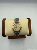 Front view of Venus wristwatch on display pillow showing gold-tone case and stretch band
