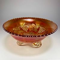 Side view of iridescent marigold carnival glass bowl on three feet