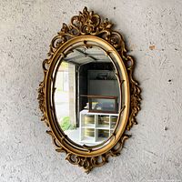 Front view of ornate gold oval mirror hanging on wall