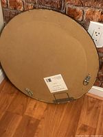 Back of round mirror showing cardboard backing and D-ring mounts
