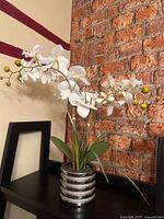 White orchid arrangement in silver-striped pot on shelf