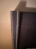 Close-up of gray wingback headboard corner showing silver nailhead trim