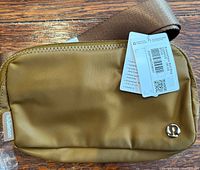 Front of green-brown Lululemon belt bag with tag and logo visible