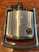 Top view of Breville Panini Press showing stainless steel lid, handle, power cord, controls