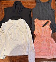 Four garments laid out: black vest, white long sleeve, black tank, coral tank