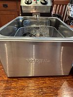 Front view of stainless steel fryer body with embossed Waring logo and basket inside