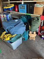 pile of tents, sleeping bags, grey tote, wooden stool