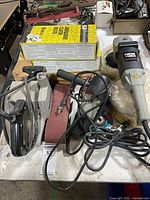 Overview showing three Porter-Cable power tools with cords plus sanding belt boxes and abrasive roll