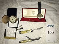 All items laid out: Drusus pocket watch, Sarcar wristwatch in box, cufflinks, three pocket knives