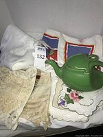 Overall lot showing green Hall teapot, stacked linens including white tablecloth, printed napkins, crocheted doilies, embroidered placemat