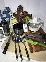 Overall view of lot with crockpot, juicer, cutting boards, utensils, graters, hot pads, knives