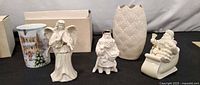 Front view of five Lenox porcelain pieces: tumbler, angel, wise man, vase, Santa in sleigh, with boxes behind