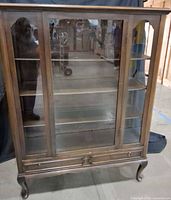 Front view showing glass double doors, shelves, drawer, legs