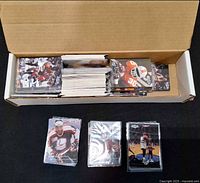 open cardboard box of assorted sports trading cards with additional sleeved stacks in front