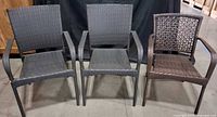 Front view of three woven patio armchairs, two gray and one brown