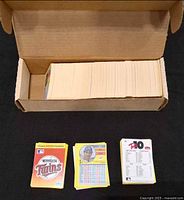 Open cardboard box filled with stacked loose baseball cards, stacks of three card types displayed in front