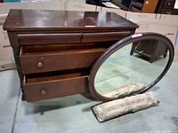 Dresser with two drawers open, oval mirror and wrapped supports in front