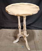Full view of white round accent table showing scalloped top, turned legs, tripod base